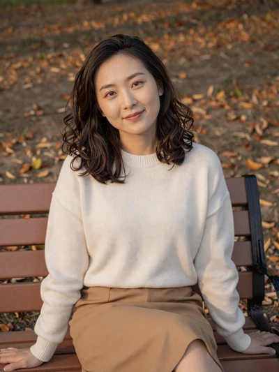 Lin sitting peacefully on a park bench surrounded by autumn foliage